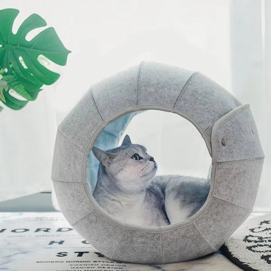 Grey felt cat cave set upright as an open ring, with a grey cat lying inside and light from the window showing through