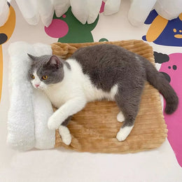 Grey and white cat lying on top of a tan ribbed plush sleeping sack laid flat, its head by the white fluffy cuff