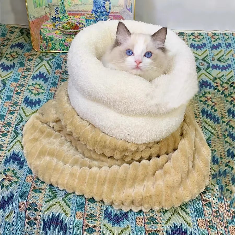 Ragdoll-type cat peeking out of a tan ribbed plush sleeping sack with a white fluffy cuff, on a patterned rug