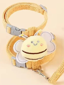 Mustard corduroy strap harness with a plush bee, grey side-release buckles and the matching lead clipped on, on a peach background