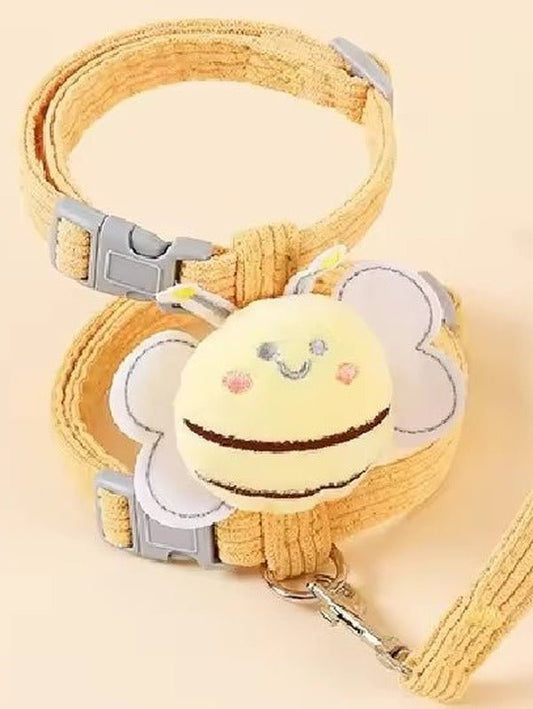 Mustard corduroy strap harness with a plush bee, grey side-release buckles and the matching lead clipped on, on a peach background