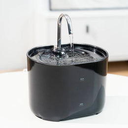 Black cat water fountain with a curved metal tap-style spout running water into the top tray