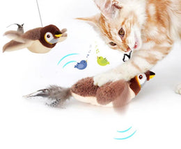 Ginger and white cat biting the plush sparrow toy on the floor, with a second sparrow hanging from a line above