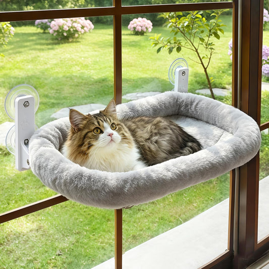 Long-haired tabby and white cat lying in a grey fluffy window bed held to the glass by suction cups, garden outside