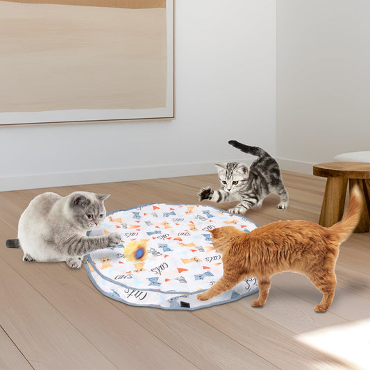 Three cats around the round cloth play pouch on a wooden floor, one pawing at the ball under the fabric