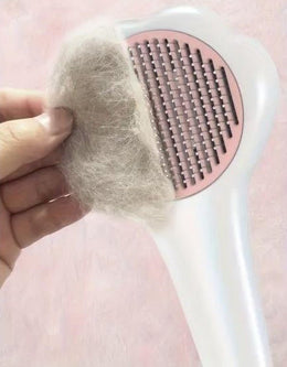 Hand lifting a pad of grey fur off the pins of the paw-shaped brush