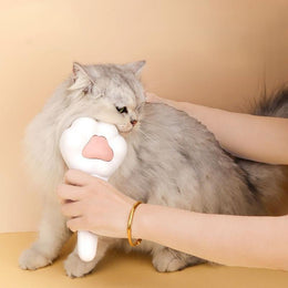 Hand brushing the cheek of a grey long-haired cat with the white paw-shaped brush
