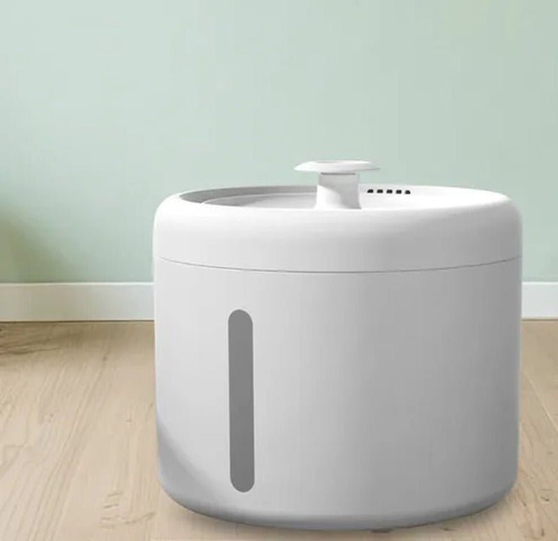 Round white cat water fountain with a small top spout and a grey water-level window on the side, on a wooden floor
