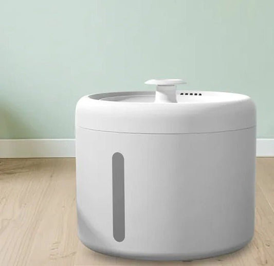 Round white cat water fountain with a small top spout and a grey water-level window on the side, on a wooden floor