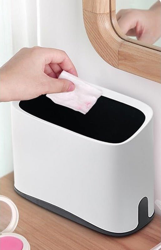 White scoop caddy used as a small bin on a wooden dressing table, with a hand dropping in a cotton pad