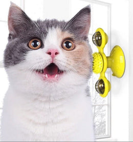 Grey and white cat with its mouth open beside a yellow windmill toy fixed to a wall by its suction cup