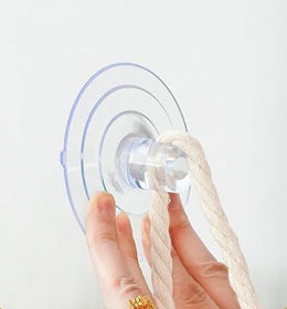 Hand pressing a clear suction cup onto glass, with a cotton rope looped through it